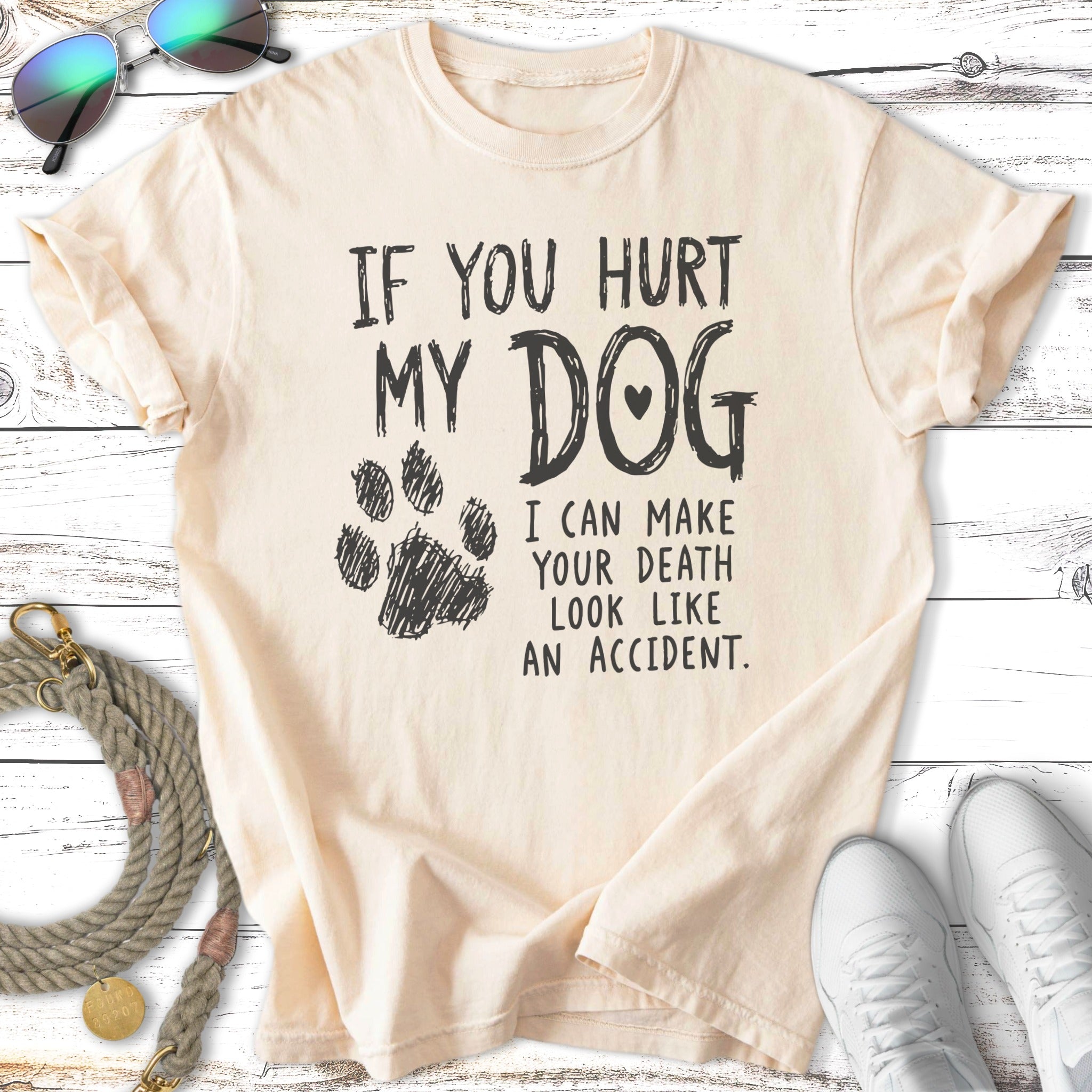 Cream t-shirt with black text and dog paw print saying "If you hurt my dog I can make your death look like an accident."