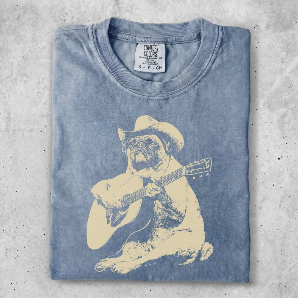 Blue t-shirt with a tan illustration of a dog wearing a cowboy hat playing a guitar.