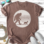 Bigfoot walking a small dog silhouette against a striped circle.