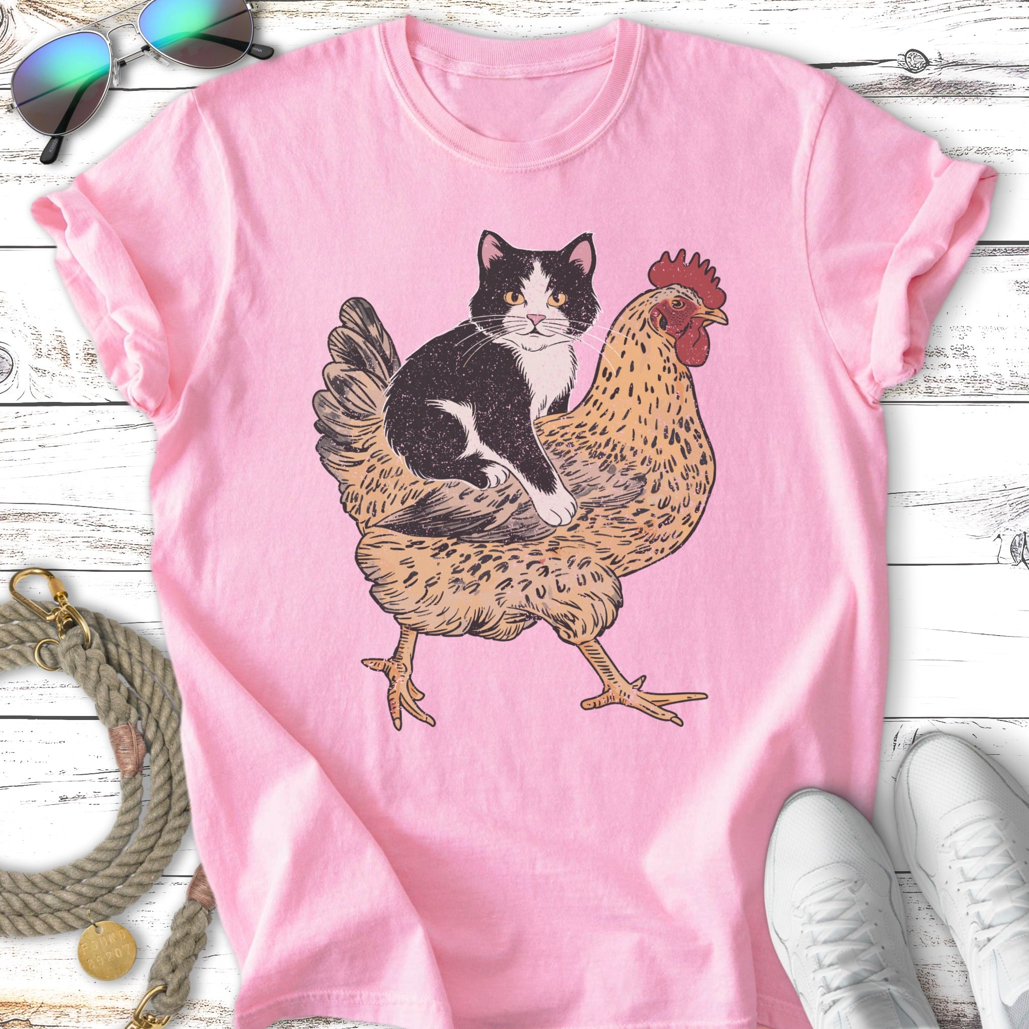 Black and white cat sitting on a brown chicken graphic on a pink t-shirt.
