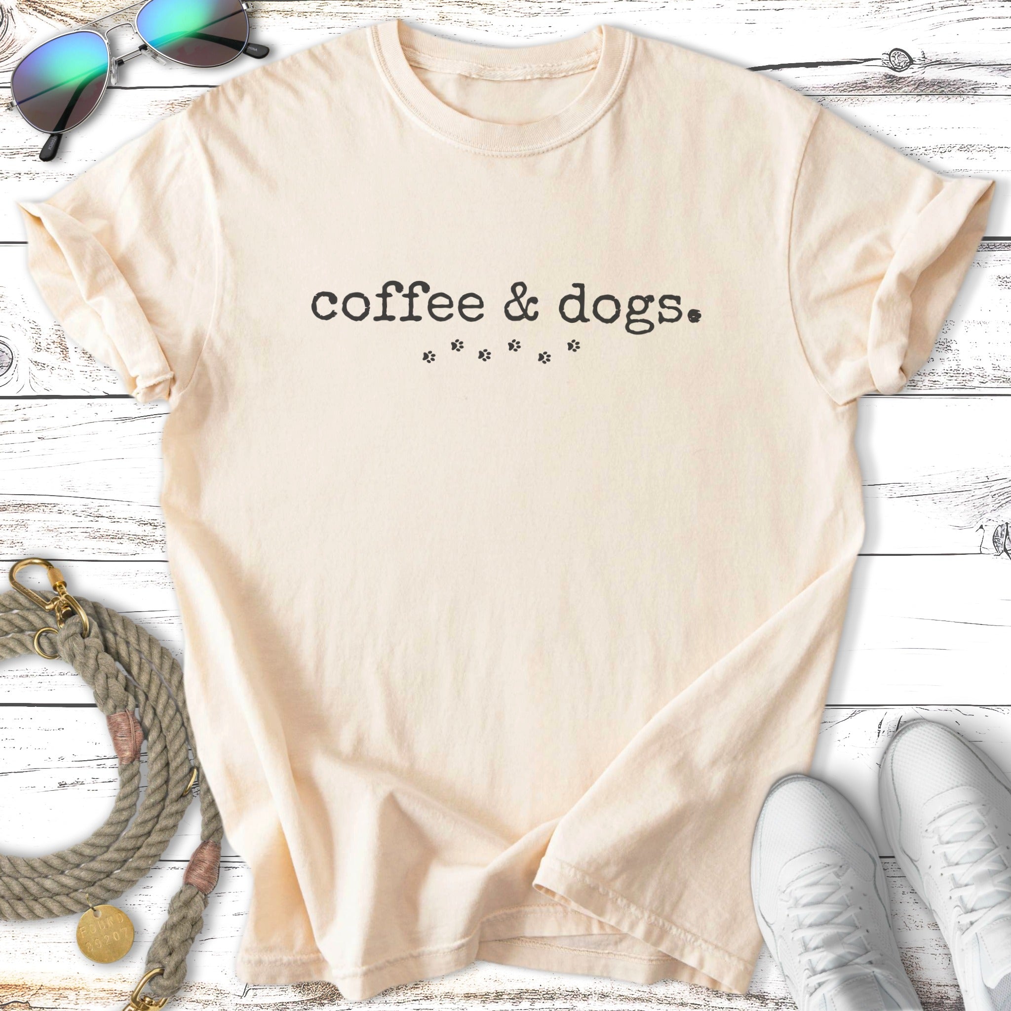 Cream t-shirt with "Coffee & Dogs" and paw prints, sunglasses, leash, and sneakers.
