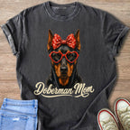 Doberman wearing heart glasses and red polka dot bow with "Doberman Mom" text.