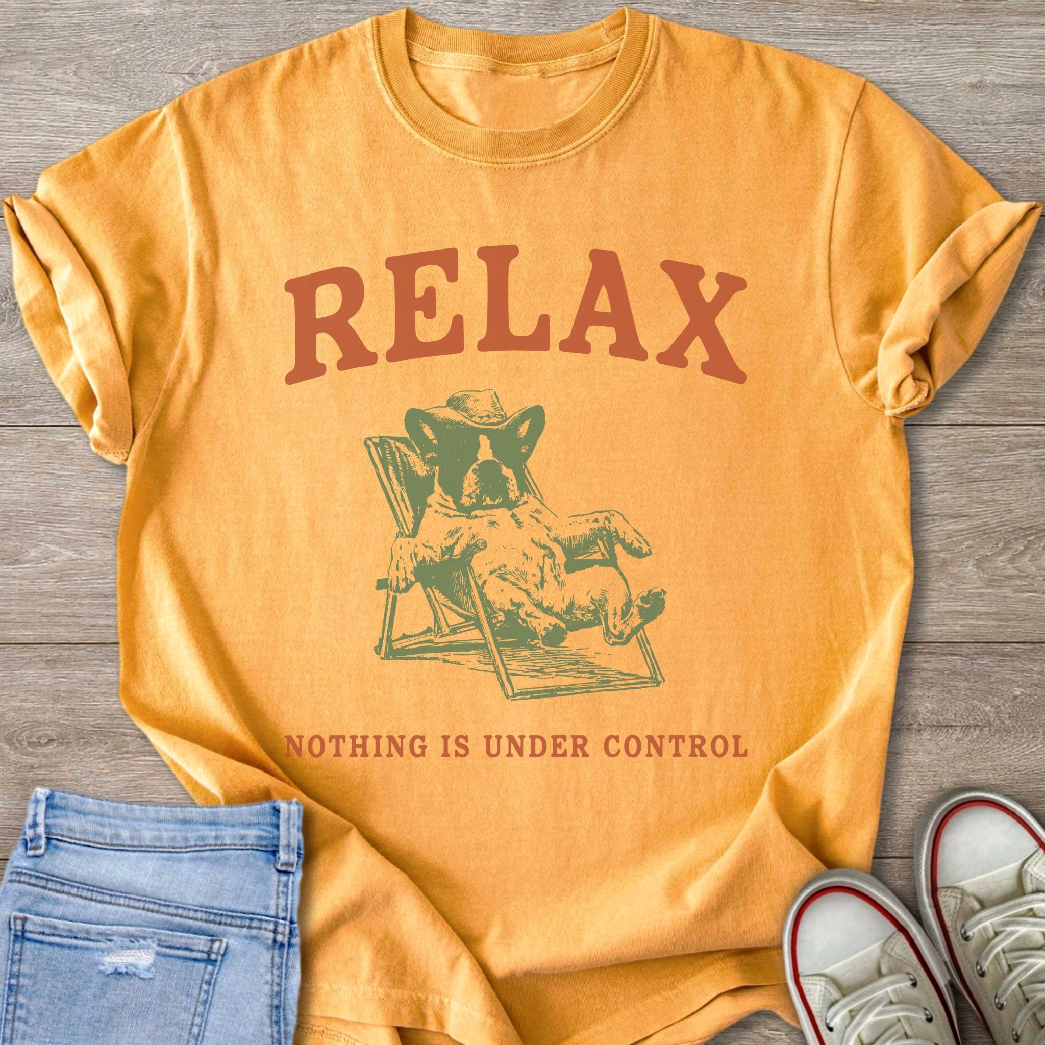Orange t-shirt with graphic of dog wearing sunglasses and hat on a lounge chair with text "RELAX NOTHING IS UNDER CONTROL".