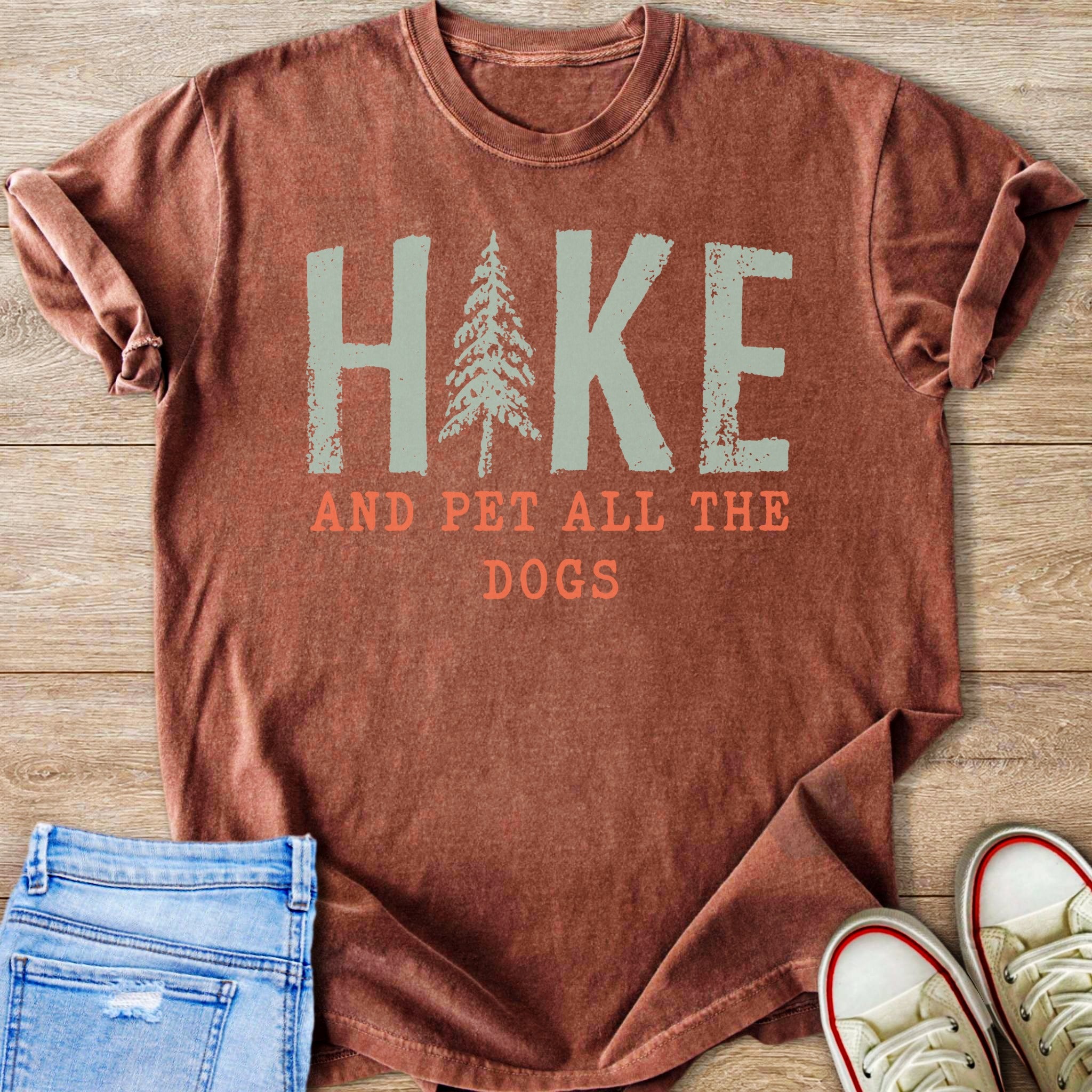Rust colored t-shirt with "Hike and pet all the dogs" graphic.