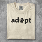 Cream t-shirt with black "adopt" text and paw print icon.