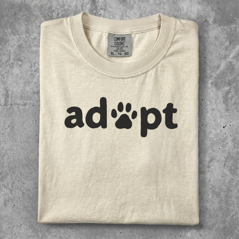 Cream t-shirt with black "adopt" text and paw print icon.