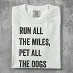 White t-shirt with black text "Run all the miles, pet all the dogs".