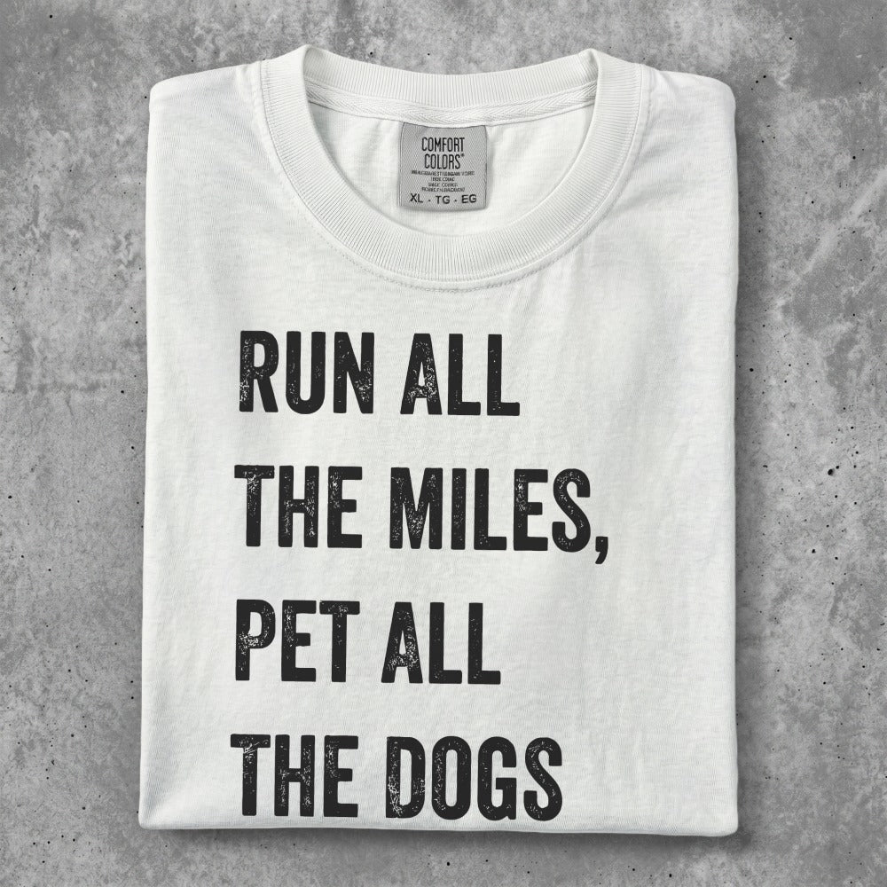 White t-shirt with black text "Run all the miles, pet all the dogs".