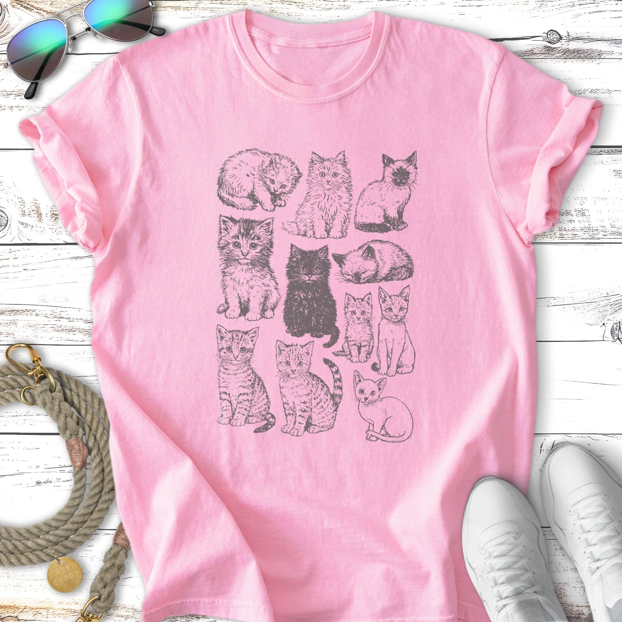 Pink t-shirt featuring a grid of twelve sketched cats in various poses.