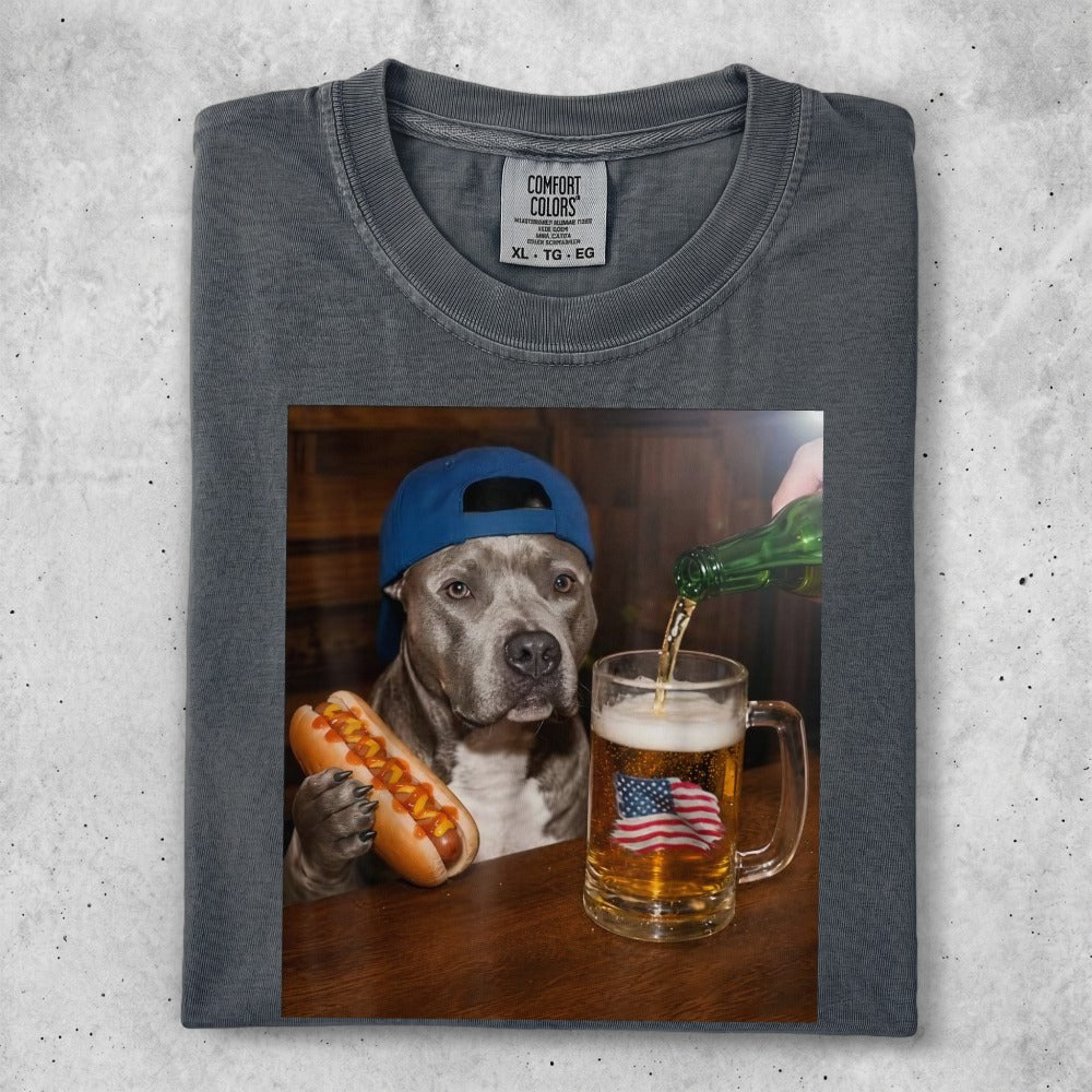 Dog in blue hat holding hot dog next to beer mug with American flag.