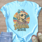 Light blue t-shirt with a graphic of a golden retriever wearing sunglasses and a bandana, with text "In My Golden ERA".