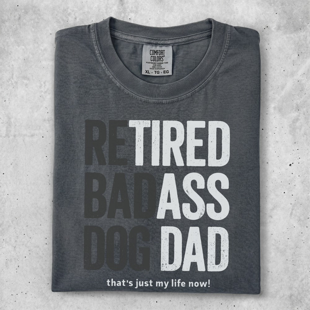 Dark grey t-shirt with "RETIRED BADASS DOG DAD" in large block letters.