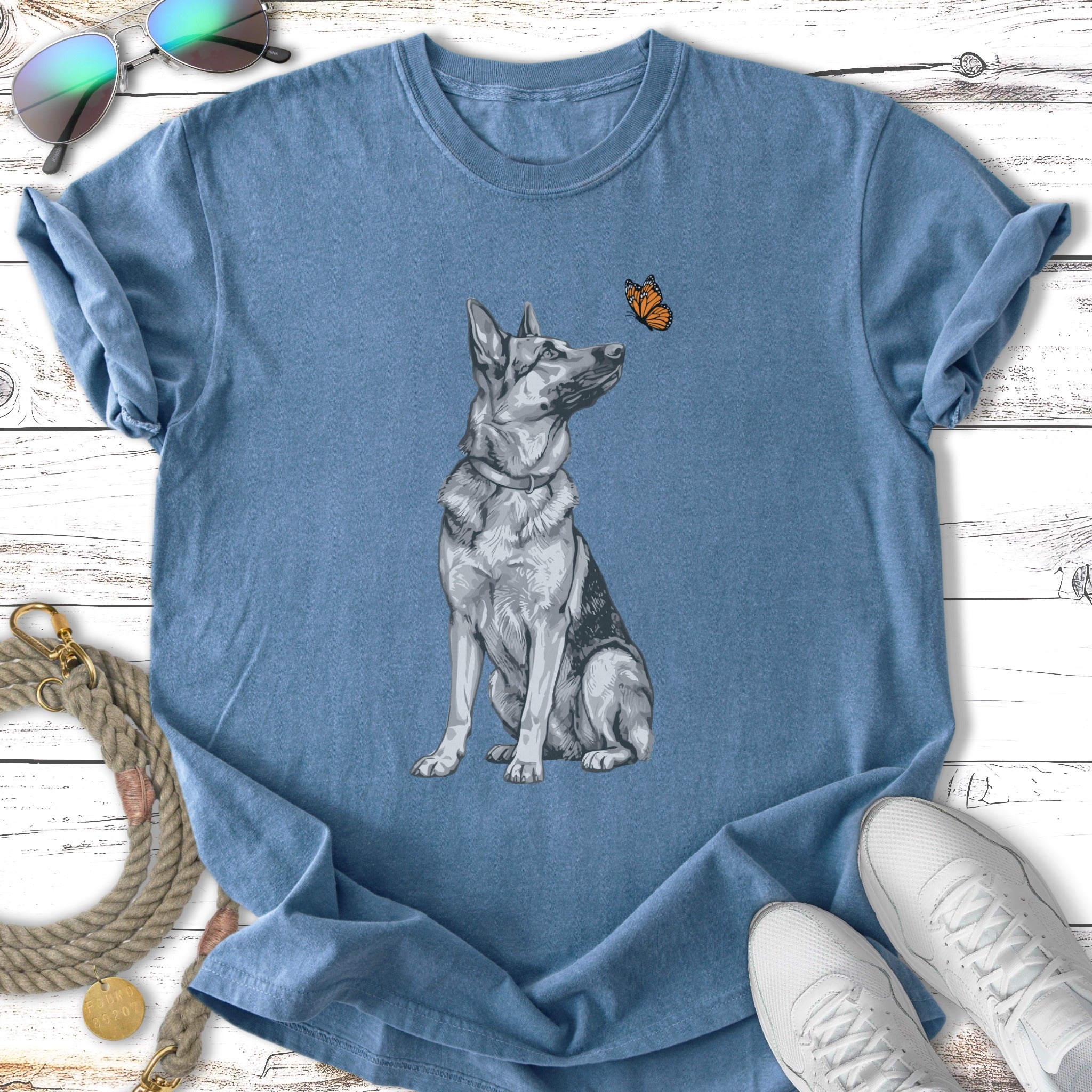 German Shepherd sitting and looking at a butterfly on a blue t-shirt.