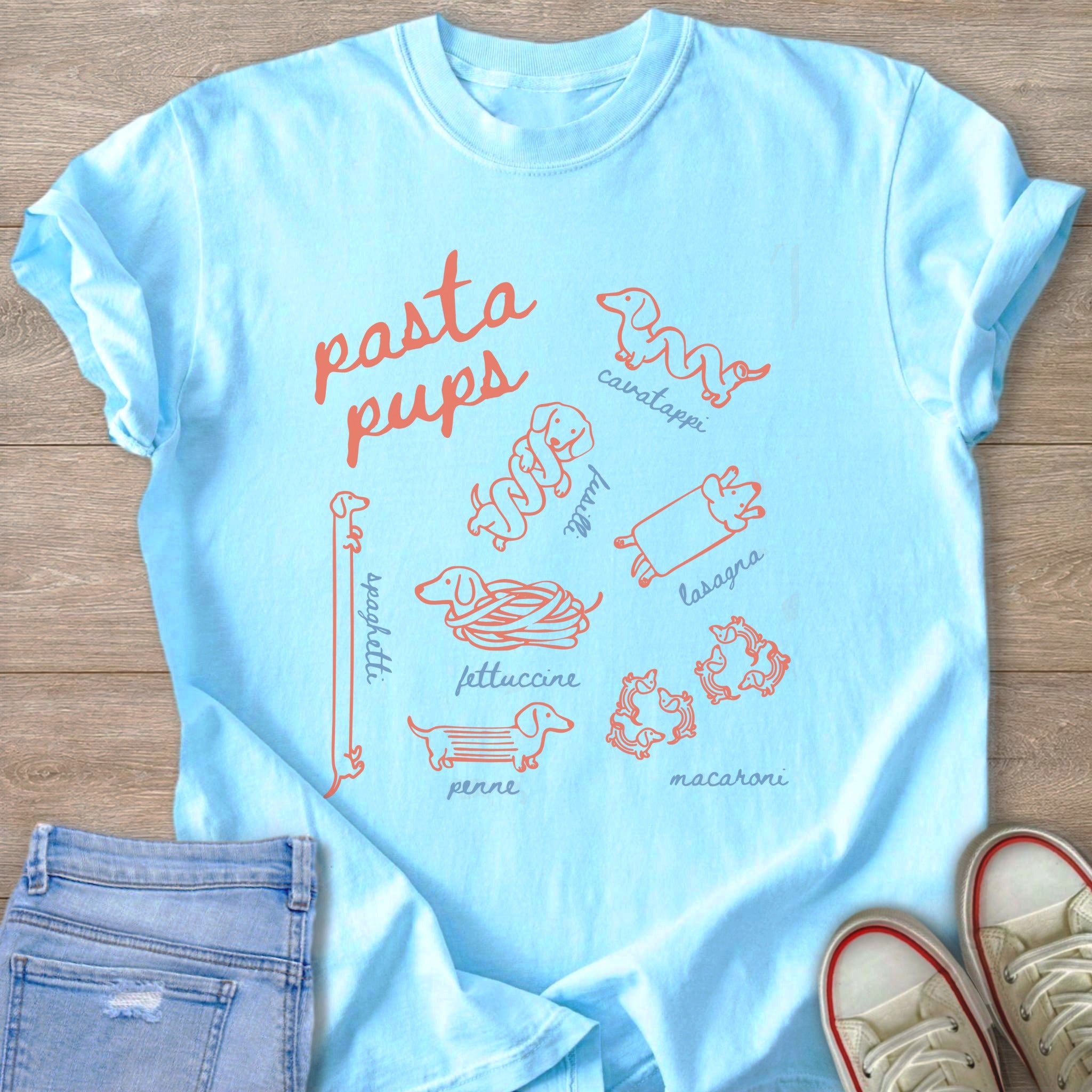 Light blue t-shirt with orange "pasta pups" text and various pasta-shaped dogs.