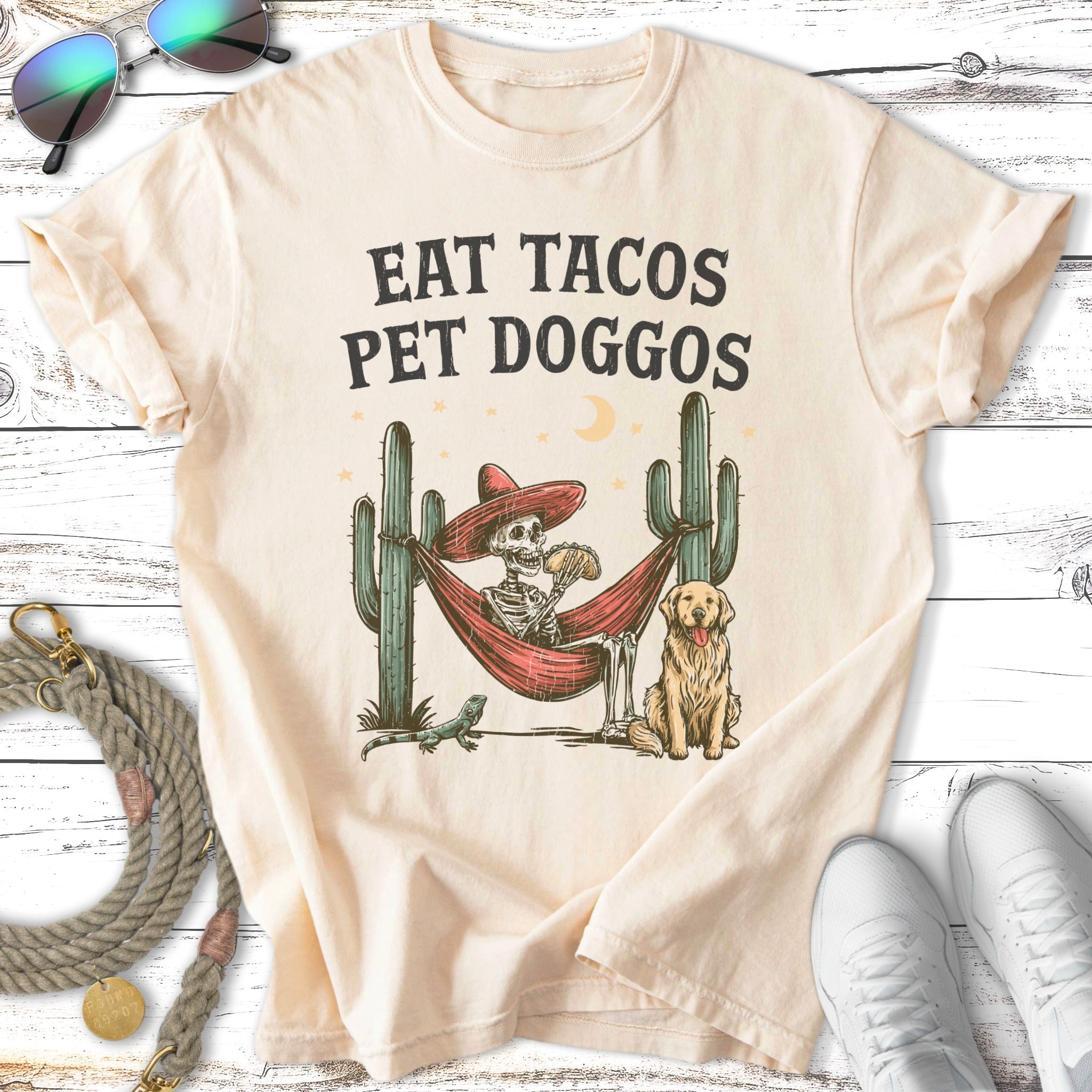 Skeleton in hammock with dog, eating taco, with cacti and moon.