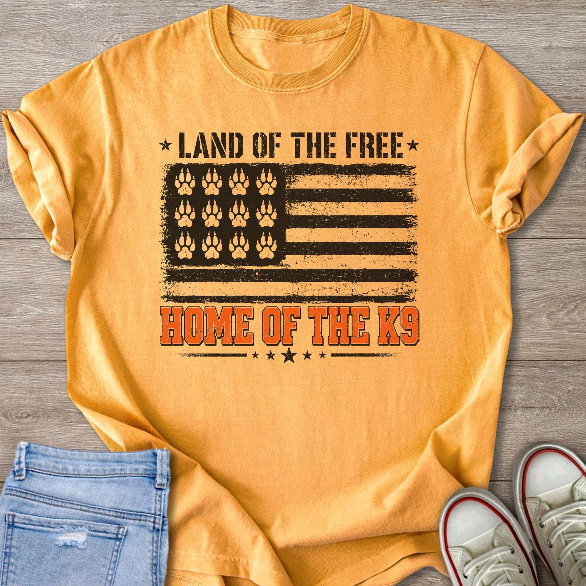 Orange t-shirt with American flag design featuring paw prints and "Land of the Free Home of the K9" text.