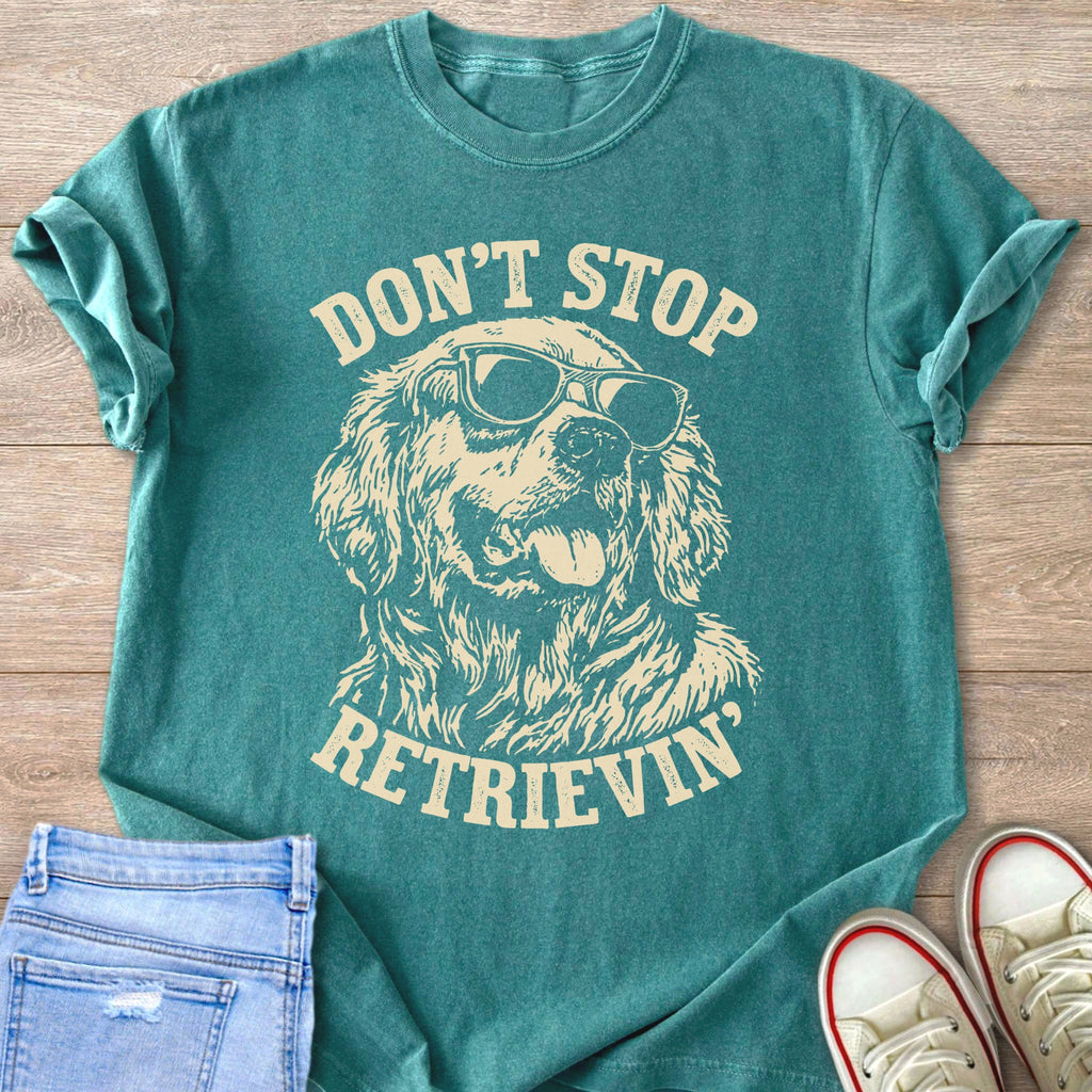 Teal t-shirt with cream graphic of dog wearing sunglasses, text reads "Don't Stop Retrieving".