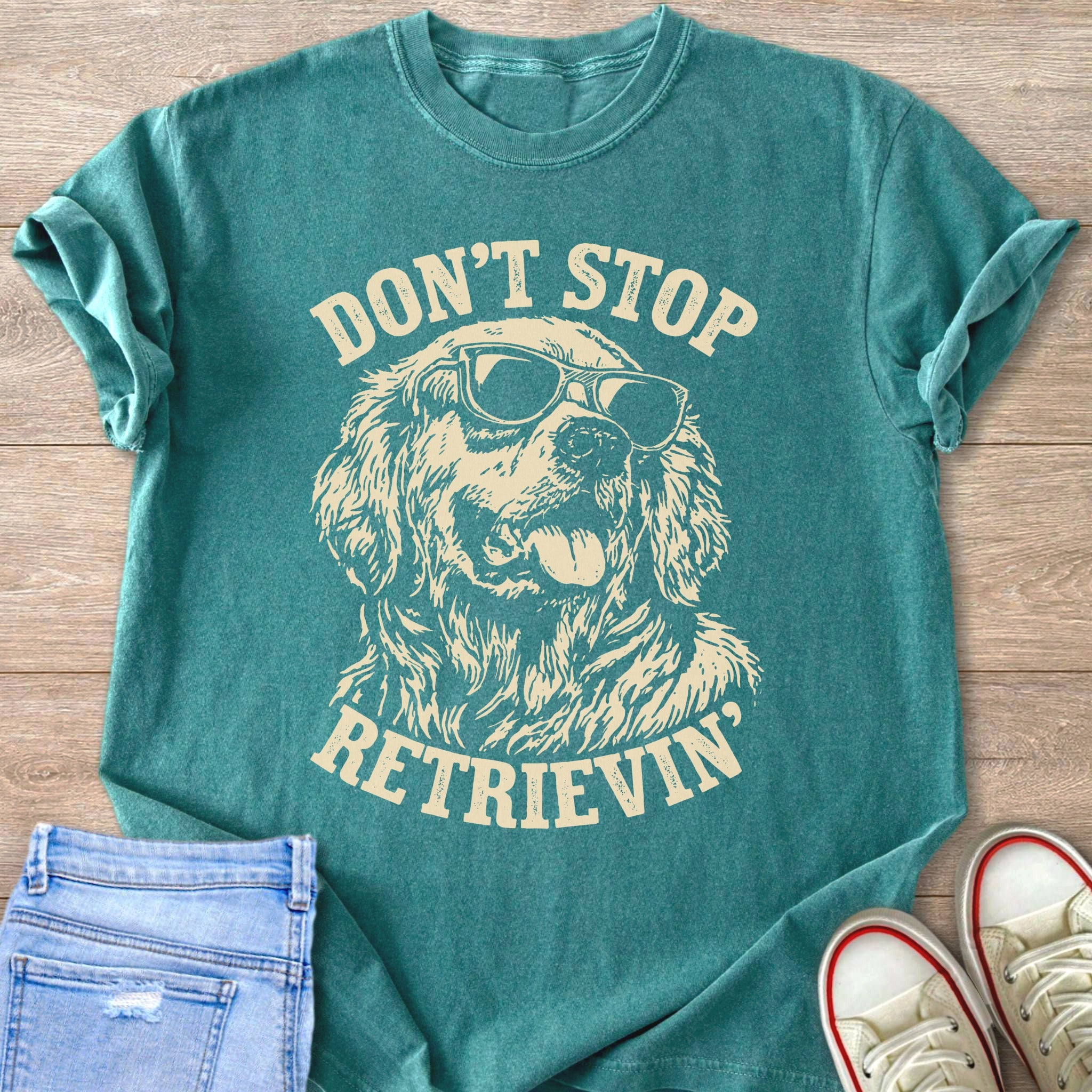 Teal t-shirt with cream graphic of dog wearing sunglasses, text reads "Don't Stop Retrieving".