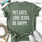 Green t-shirt with "Pet Cats. Love Jesus. Be Happy." text.