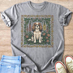 Cavalier King Charles Spaniel dog sitting amidst flowers and ivy on gray t-shirt.