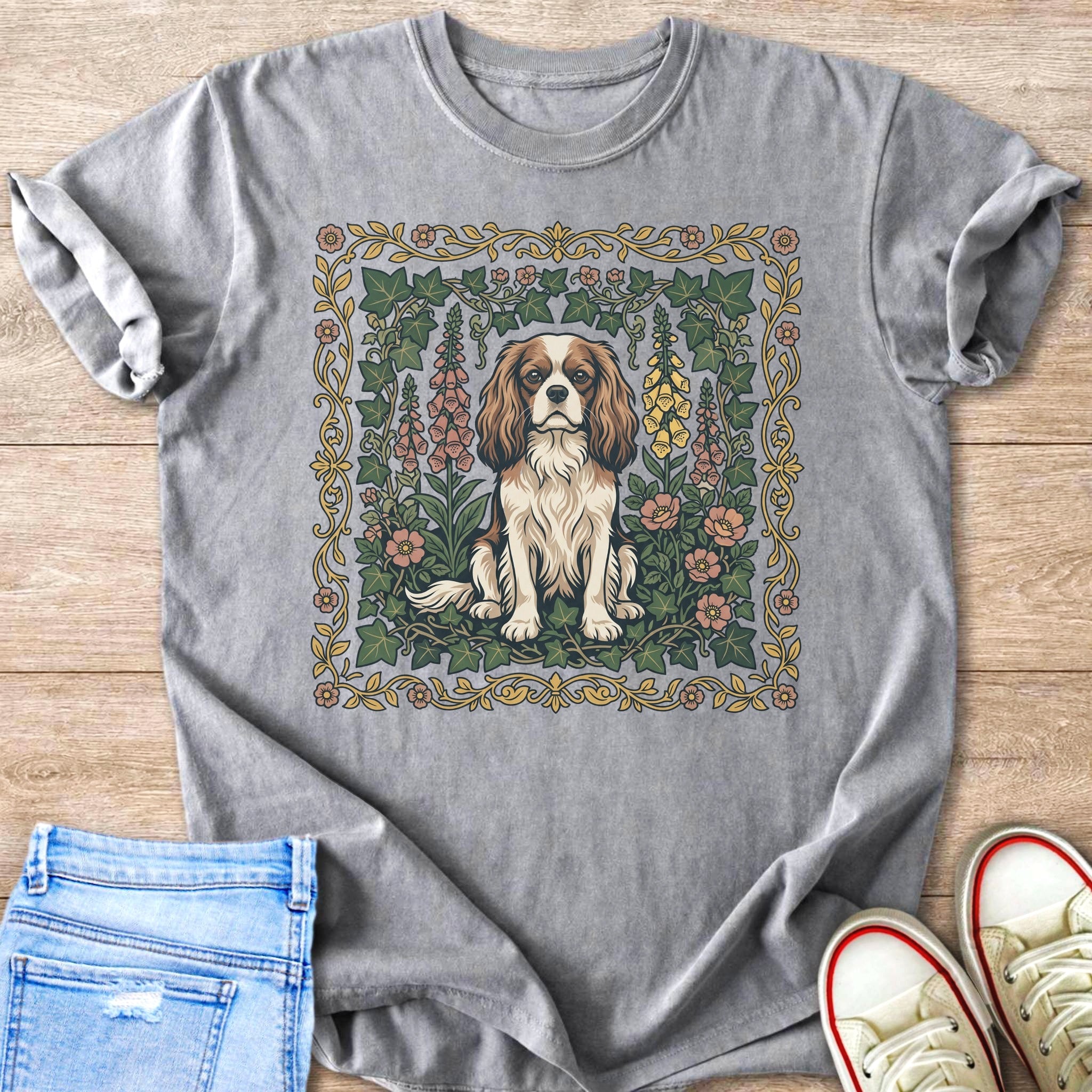Cavalier King Charles Spaniel dog sitting amidst flowers and ivy on gray t-shirt.
