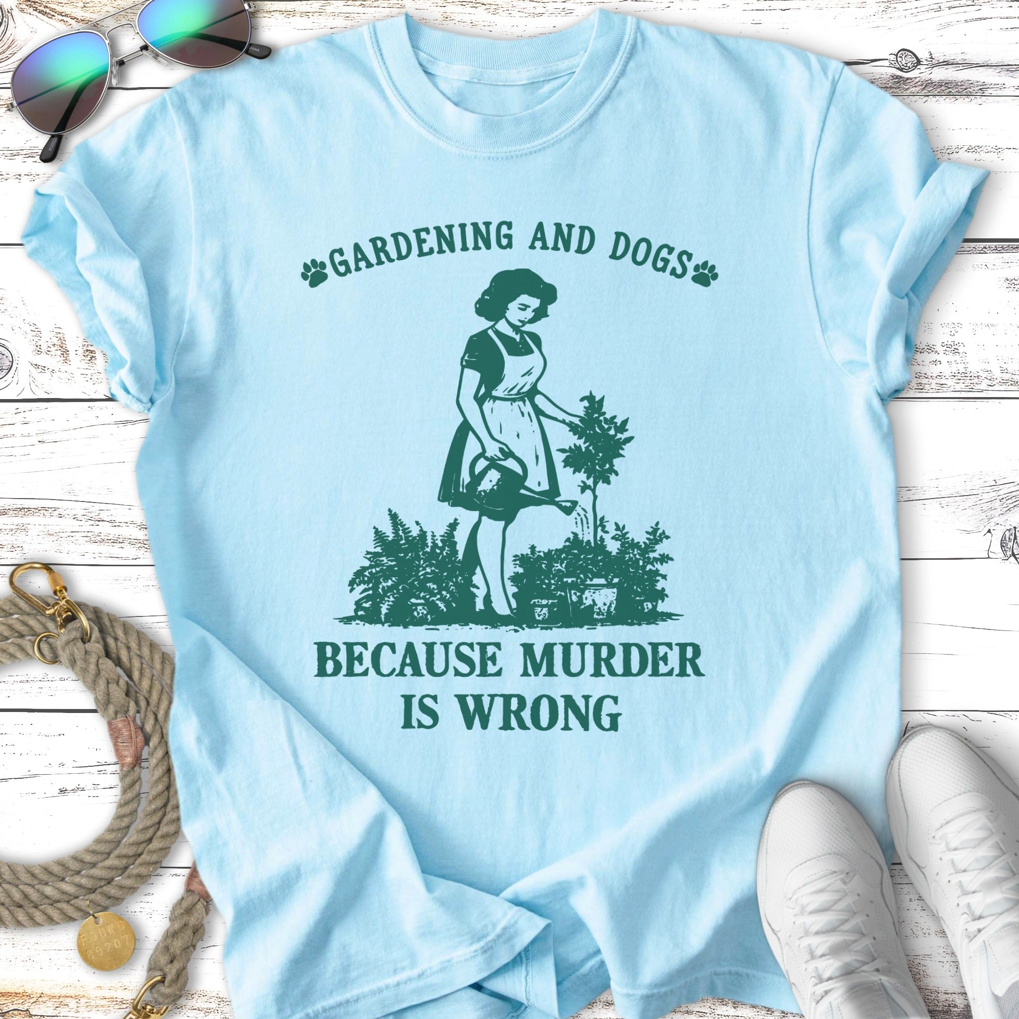 Light blue t-shirt with "Gardening and Dogs" and woman watering plants.