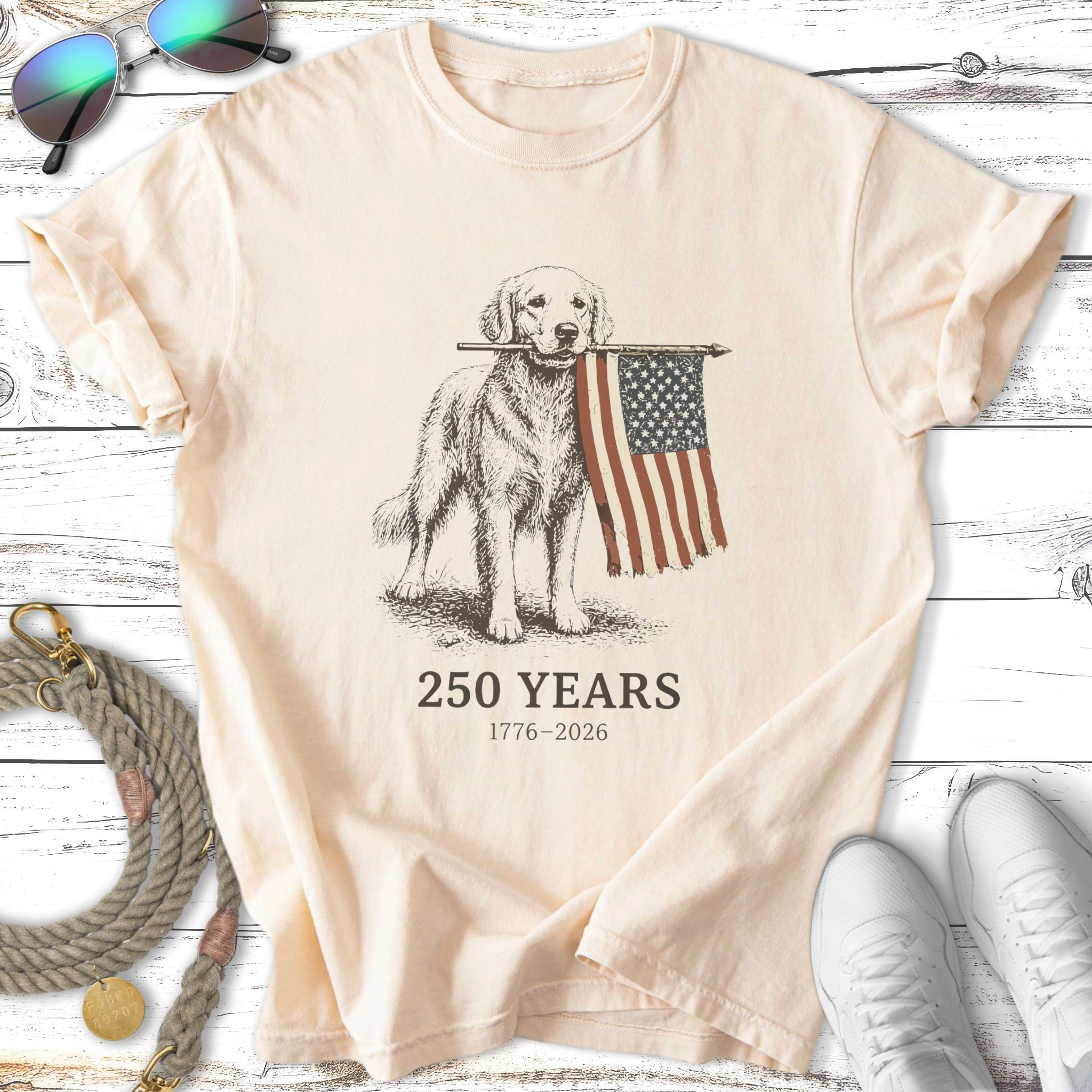 Golden retriever holding an American flag, with text "250 YEARS 1776-2026".