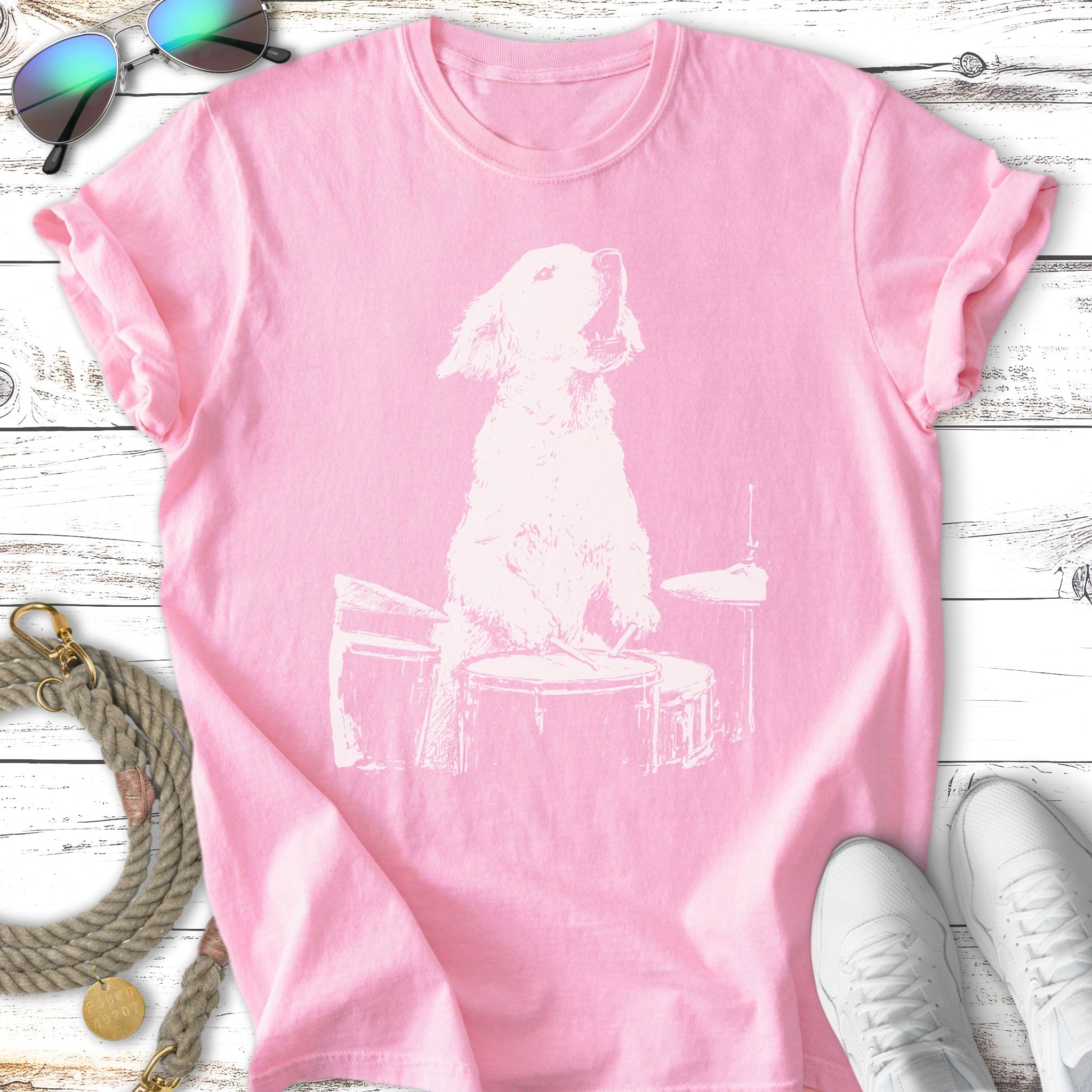 White line drawing of a dog playing drums on a pink t-shirt.