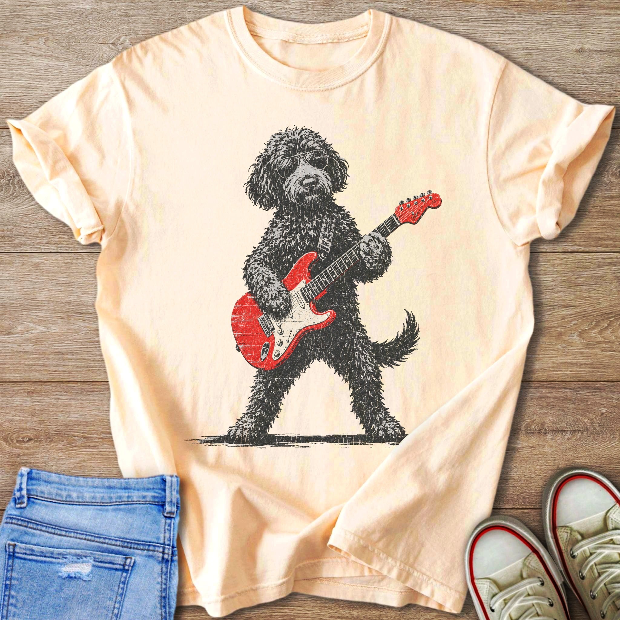 Black poodle with sunglasses playing a red electric guitar on a peach t-shirt.