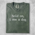 Olive green t-shirt with white text that reads "hold on, i see a dog".