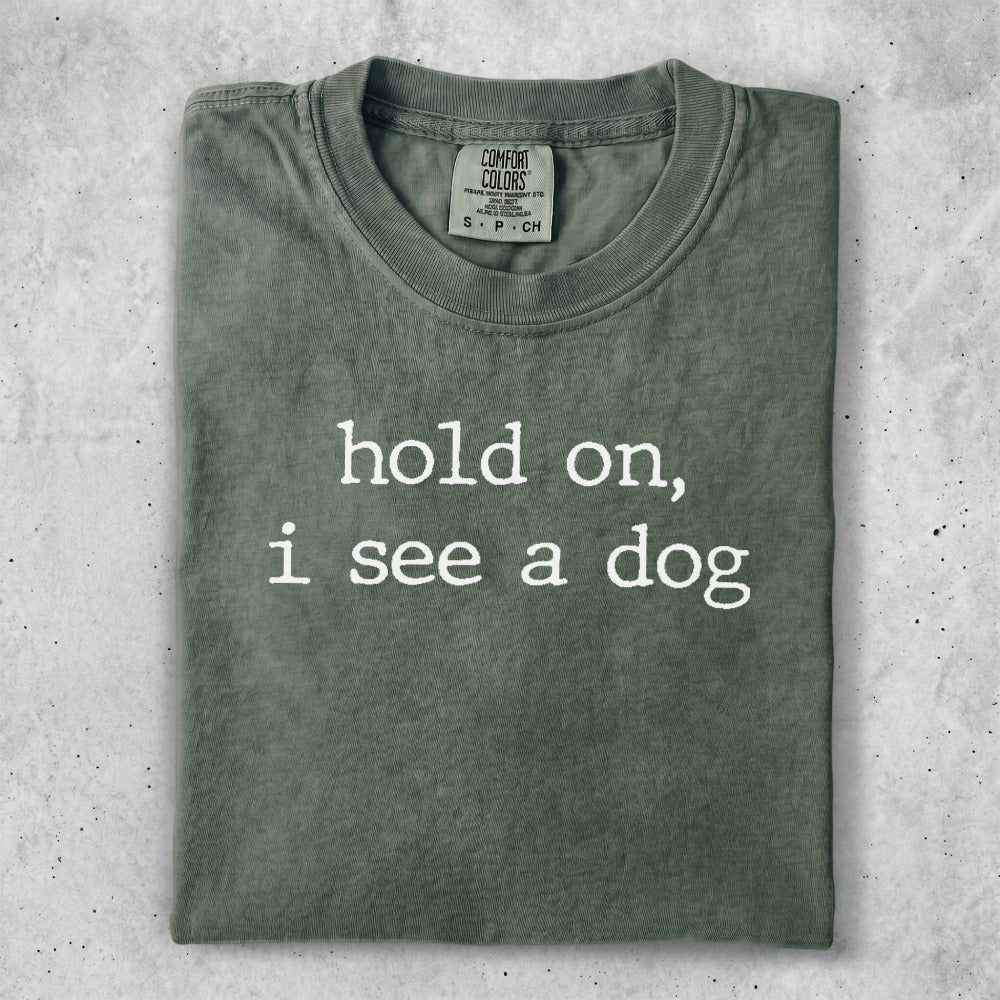 Olive green t-shirt with white text that reads "hold on, i see a dog".