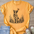 German Shepherd looking at a butterfly in a sketched floral scene on an orange t-shirt.
