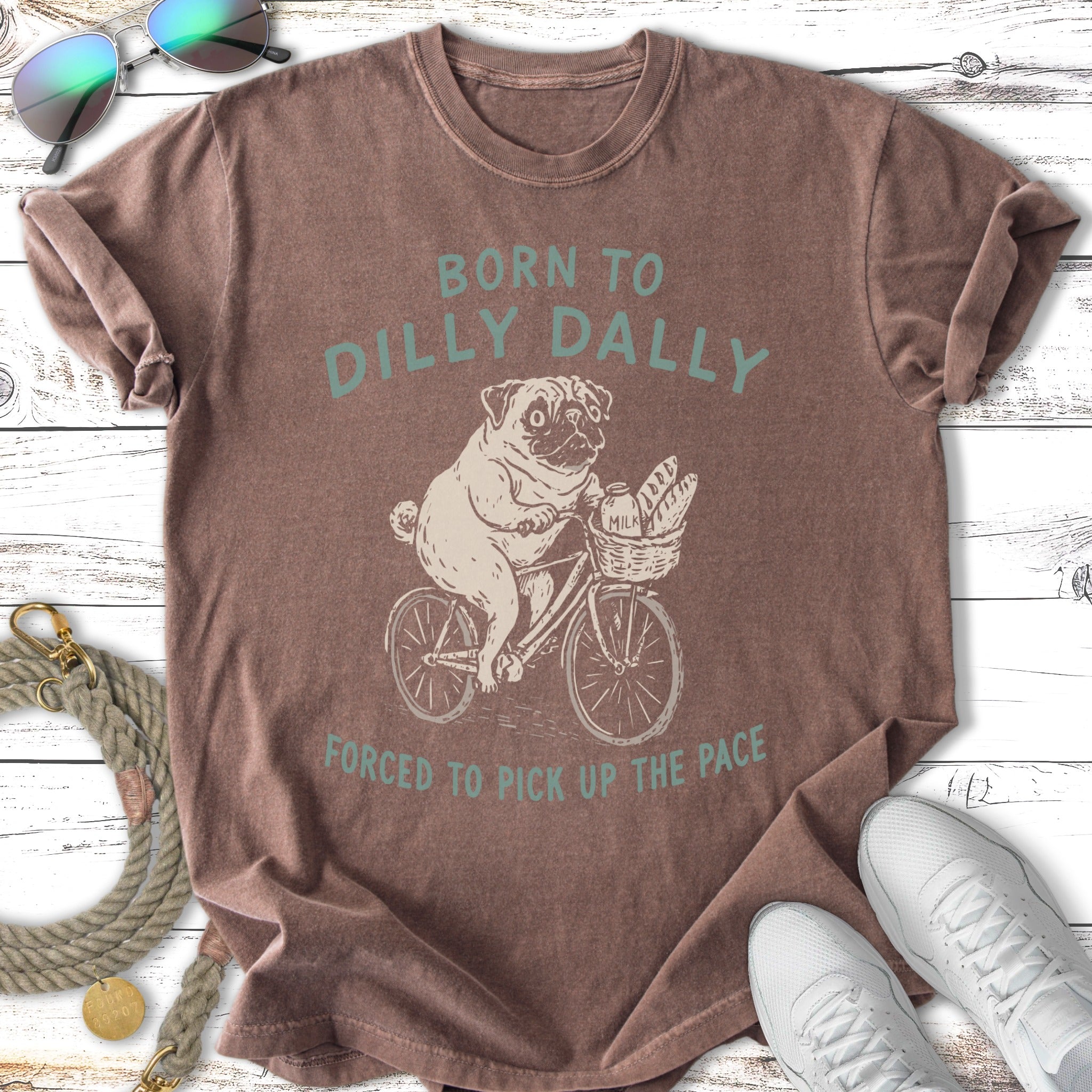 Brown t-shirt with pug on bicycle and text "BORN TO DILLY DALLY FORCED TO PICK UP THE PACE".