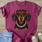 Dachshund wearing large leopard print glasses and diamond necklace on maroon t-shirt.