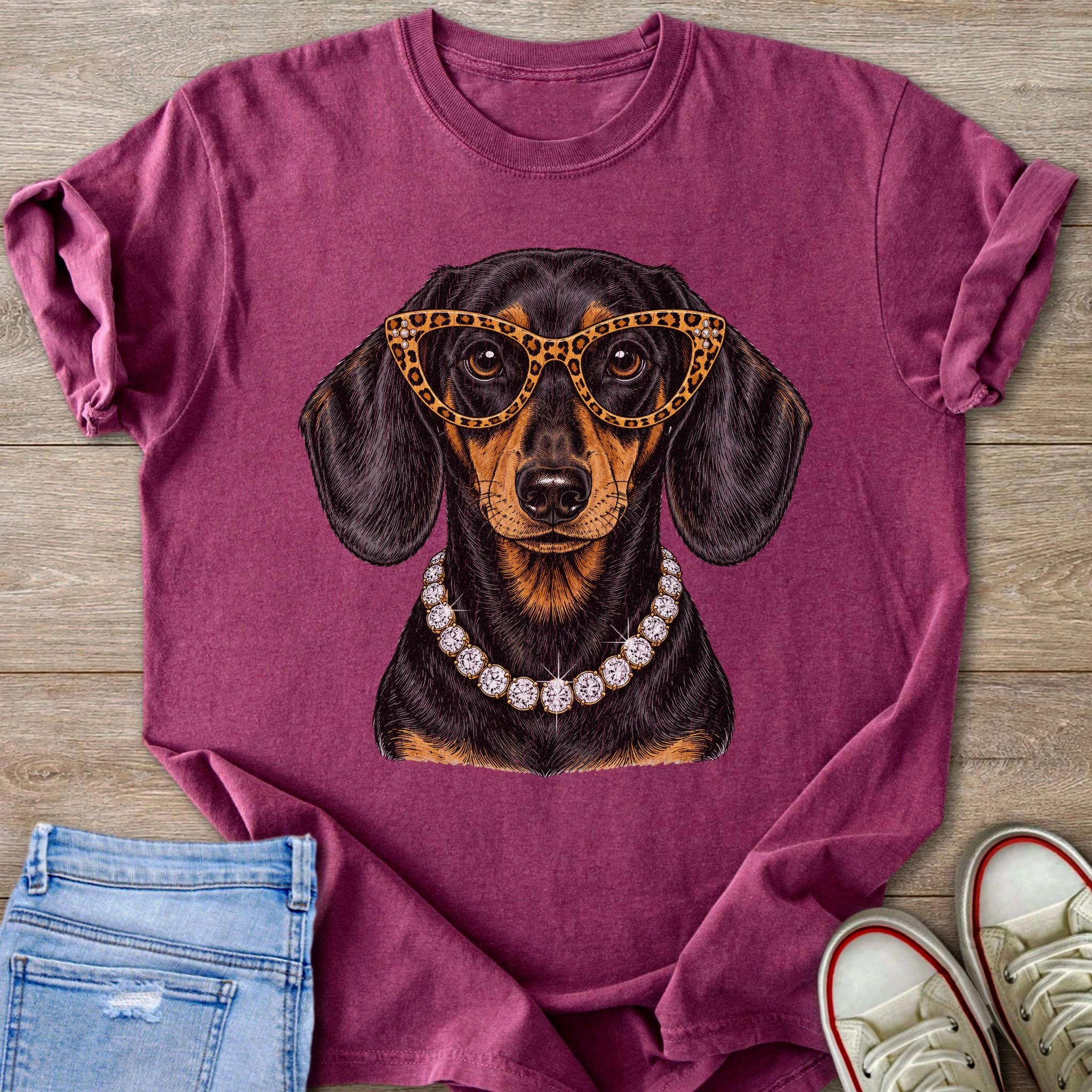 Dachshund wearing large leopard print glasses and diamond necklace on maroon t-shirt.