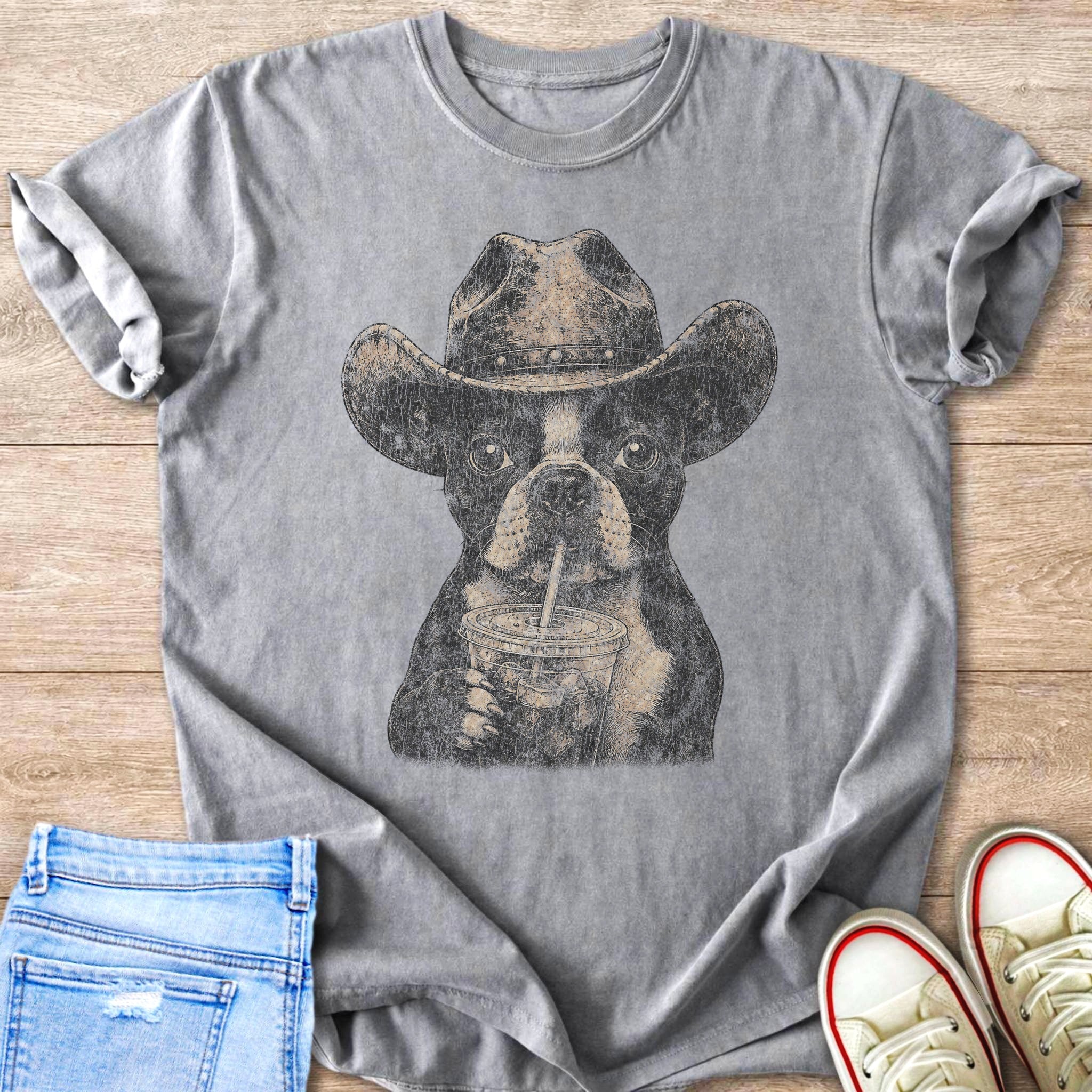 Boston Terrier in cowboy hat drinking from a straw cup, graphic tee.