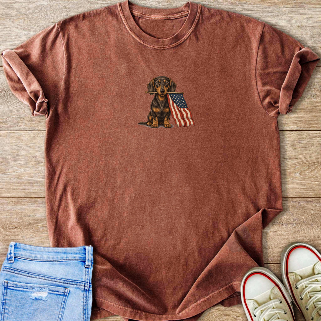 Dachshund holding USA flag centered on rustic red t-shirt.