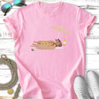 Pink t-shirt with cartoon dachshund in a hot dog bun under a beach umbrella.