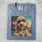 Dog wearing sunglasses drinks from a cup, printed on a light blue t-shirt.