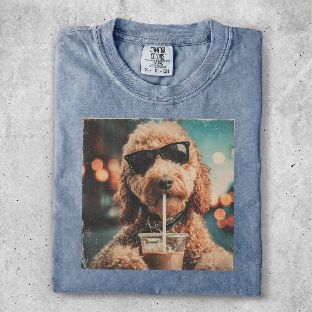 Dog wearing sunglasses drinks from a cup, printed on a light blue t-shirt.
