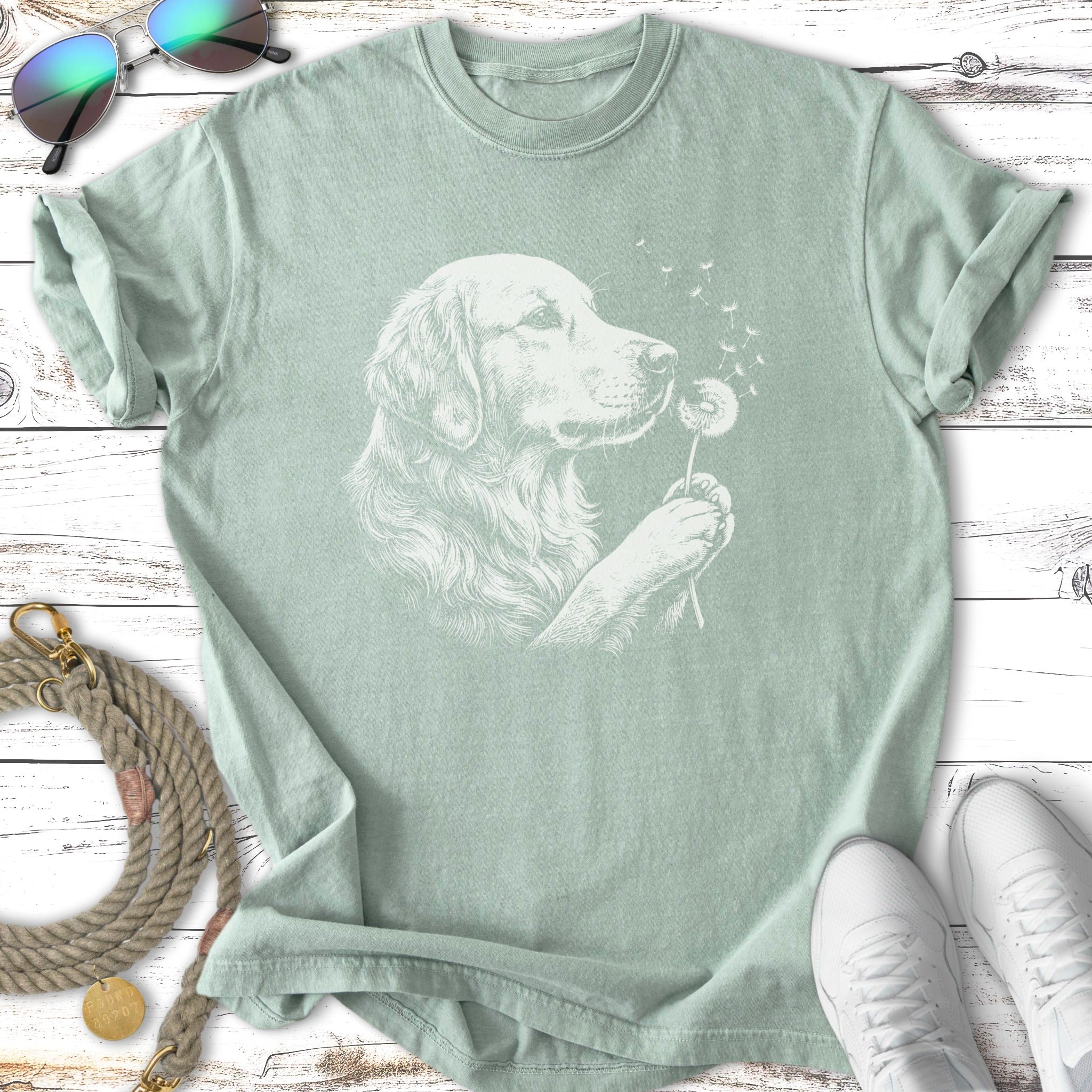 Line drawing of a golden retriever blowing dandelion seeds on a light green t-shirt.