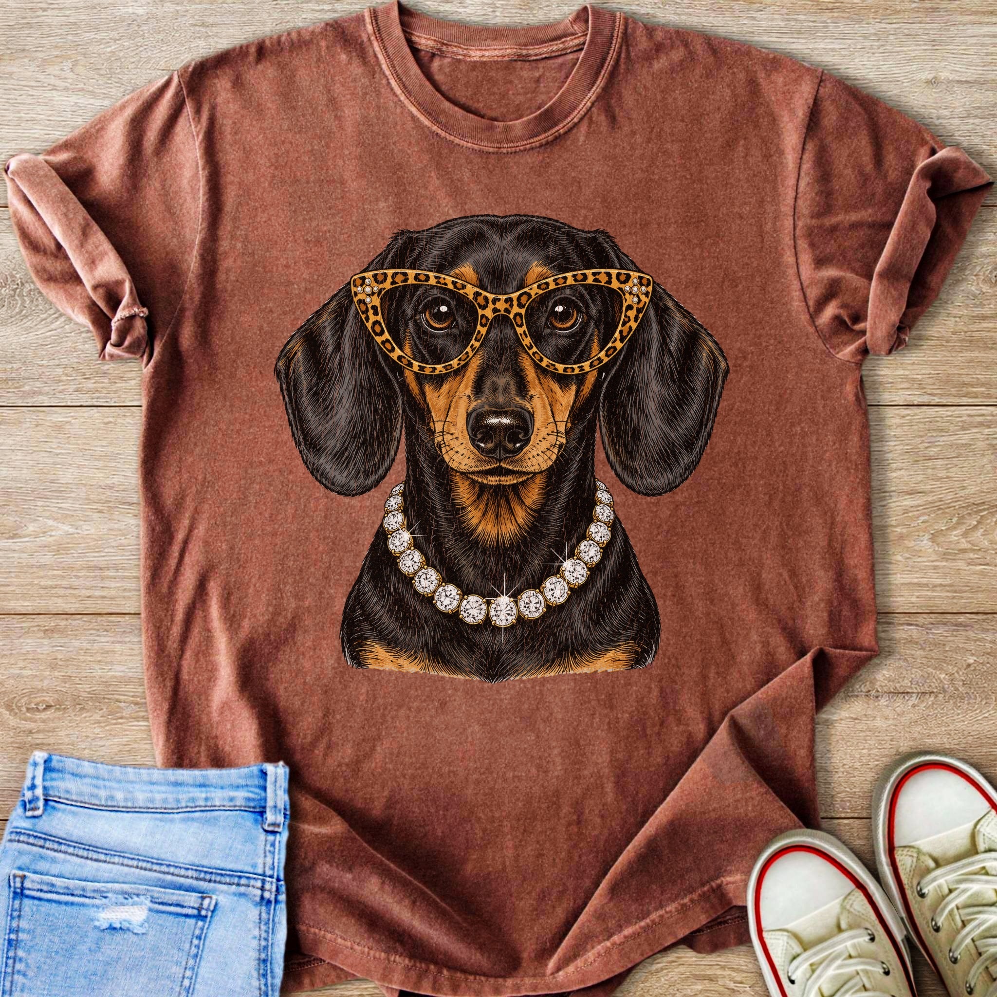 Dachshund wearing leopard glasses and diamond necklace graphic on rust t-shirt.