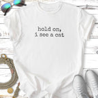White t-shirt with black text "hold on, i see a cat".