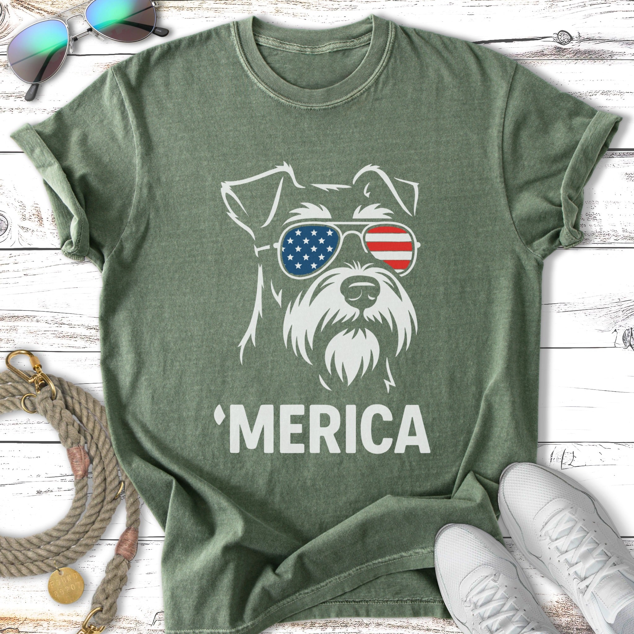 White silhouette of a schnauzer wearing American flag sunglasses on a green t-shirt.