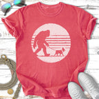 Bigfoot walking a dog with a distressed sun graphic.