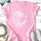 Labrador retriever puppy holding a dandelion puff with its mouth on a pink t-shirt.