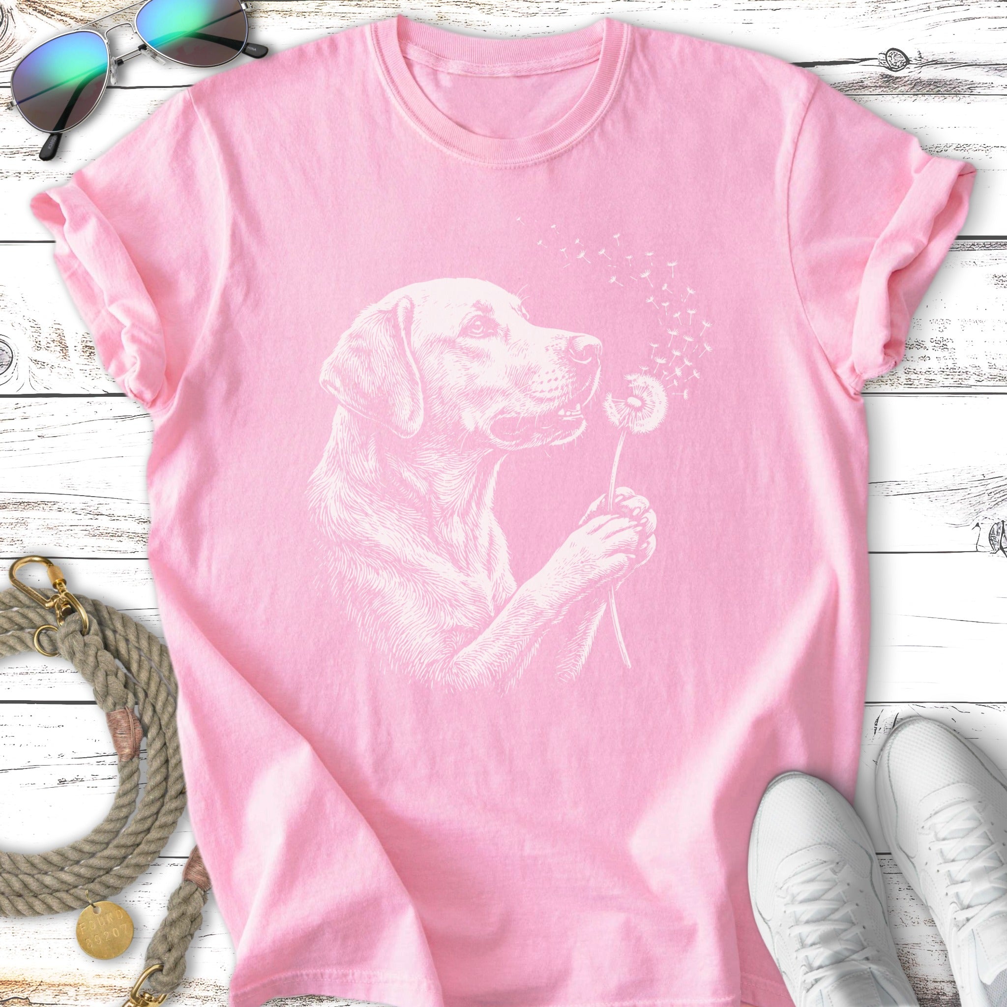 Labrador retriever puppy holding a dandelion puff with its mouth on a pink t-shirt.
