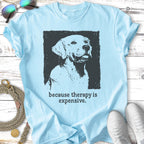 Light blue t-shirt with a black dog illustration and text "because therapy is expensive."
