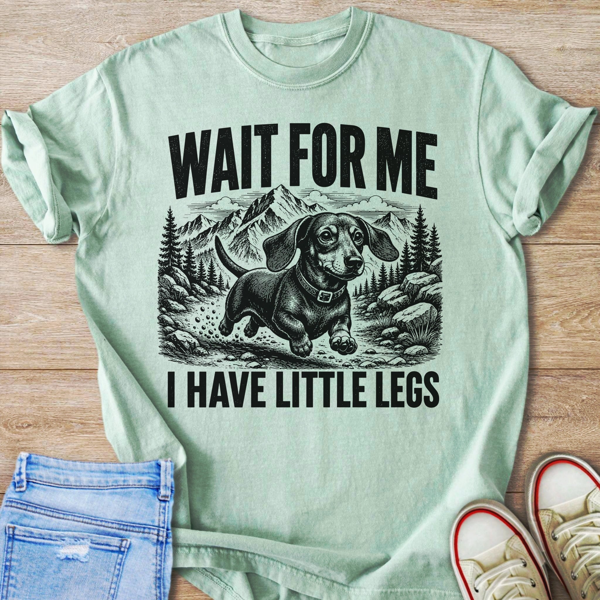 Dachshund graphic with text "WAIT FOR ME I HAVE LITTLE LEGS" on pale green shirt.