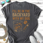 T-shirt with text "I'll be in the backyard with my dog," whiskey glass, and cigar.